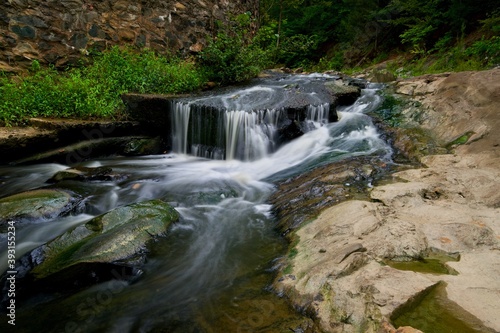 Small waterfall pouring over rocky cascades next to forest © Kelly