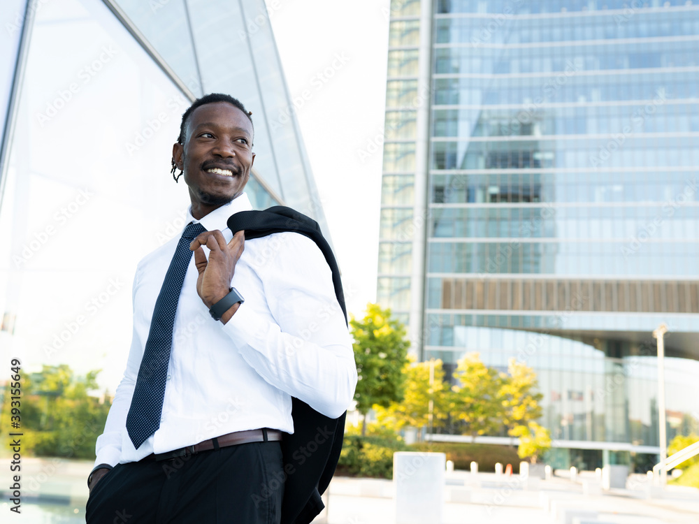 Handsome African American male entrepreneur in elegant shirt standing with jacket on shoulder in downtown and looking away Handsome African American male entrepreneur in elegant shirt standing with jacket on shoulder in downtown and looking away