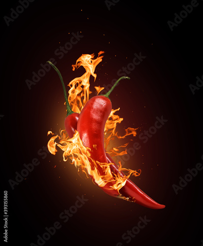 Two red chili peppers in a burning flame close-up on a black background. photo