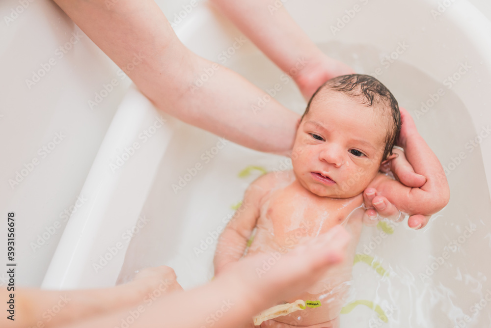 From above unrecognizable parent washing crying newborn baby in warm water in basin at home From above unrecognizable parent washing crying newborn baby in warm water in basin at home