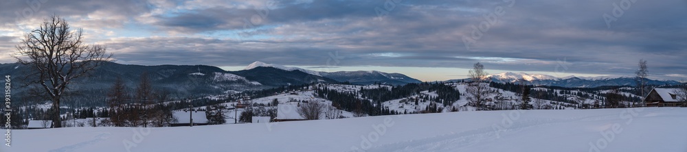 Small alpine village and winter snowy mountains in first sunrise sunlight around, Voronenko, Carpathian, Ukraine. Trace on freshly trodden path through snow drifts.