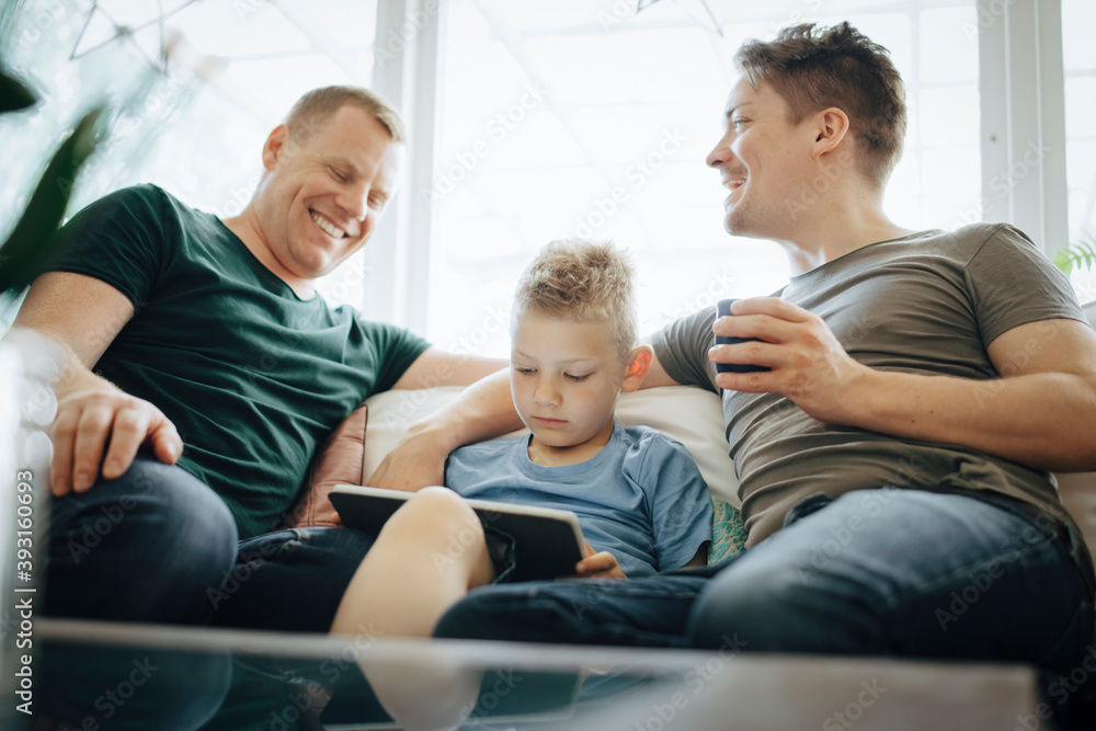 Smiling homosexual fathers talking while son using digital tablet at home Smiling homosexual fathers talking while son using digital tablet at home