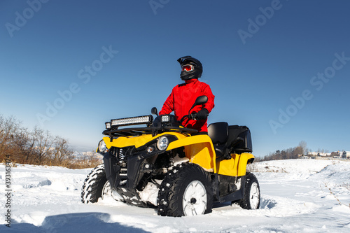 Young man driver on the ATV quad bike stand in heavy snow with deep wheel track. Moto winter sports.