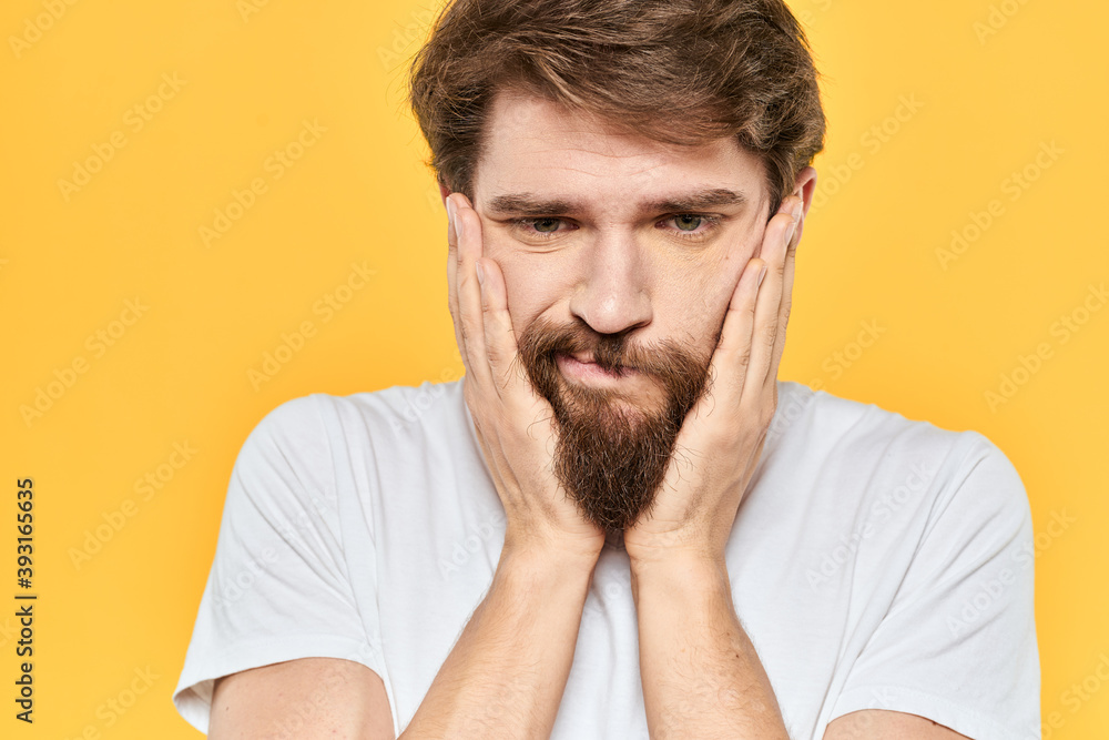 Man in white t-shirt emotions studio gestures with hands displeased facial expression yellow background Man in white t-shirt emotions studio gestures with hands displeased facial expression yellow background