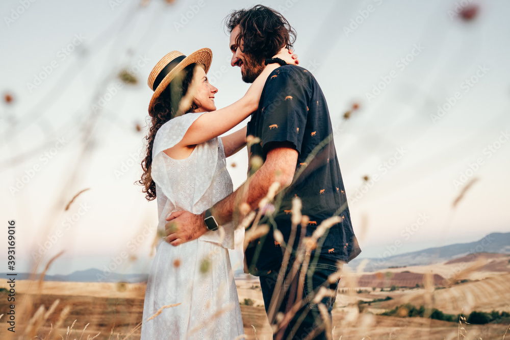 Obraz premium a boy and a girl in love embracing at summer sunset seen through the scrub of a wheat field