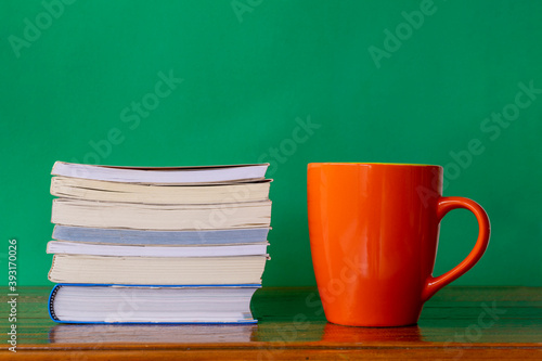 orange mug with stack of books on rustic table and green background photo