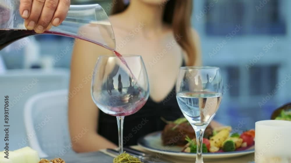 Red wine is pouring into the wine glass. the waiter is filling guest's glass with wine in a restaurant. 4K. Red wine is pouring into the wine glass. the waiter is filling guest's glass with wine in a restaurant. 4K.