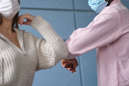 young businesswoman wearing mask bumping elbows with African-American colleague as contactless greeting in post pandemic office. selective focus