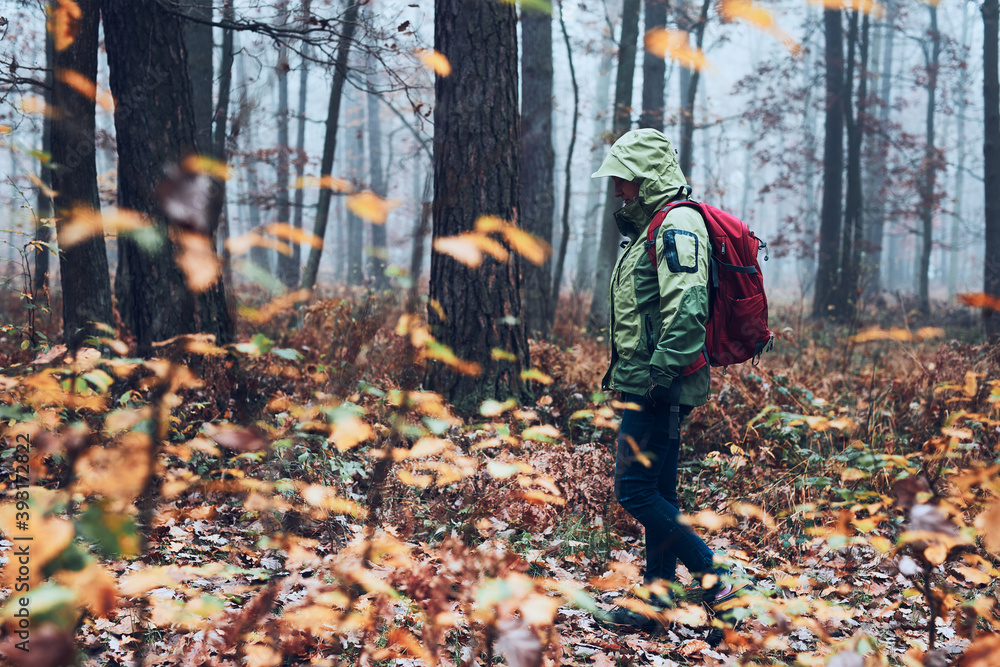 Woman with backpack wandering around a forest on autumn cold day. Side view of middle age active woman going along forest path actively spending time Woman with backpack wandering around a forest on autumn cold day. Side view of middle age active woman going along forest path actively spending time