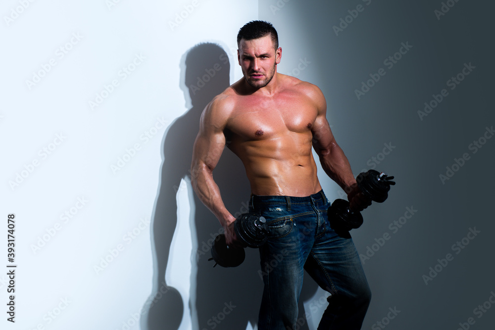 Handsome muscular man with dumbbell. Sexy shirtless young male fitness model. Bare torso of a young guy with strong chest lifting exercising dumbbells on grey background. Handsome muscular man with dumbbell. Sexy shirtless young male fitness model. Bare torso of a young guy with strong chest lifting exercising dumbbells on grey background.