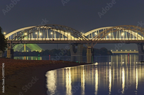 Three illuminated bridges at night. Picturesque landscape of Dnipro River with arched Railway bridge, Darnytskyi Rail and road Bridge. Pivdennyi Bridge in the background. Scenic evening landscape © evgenij84