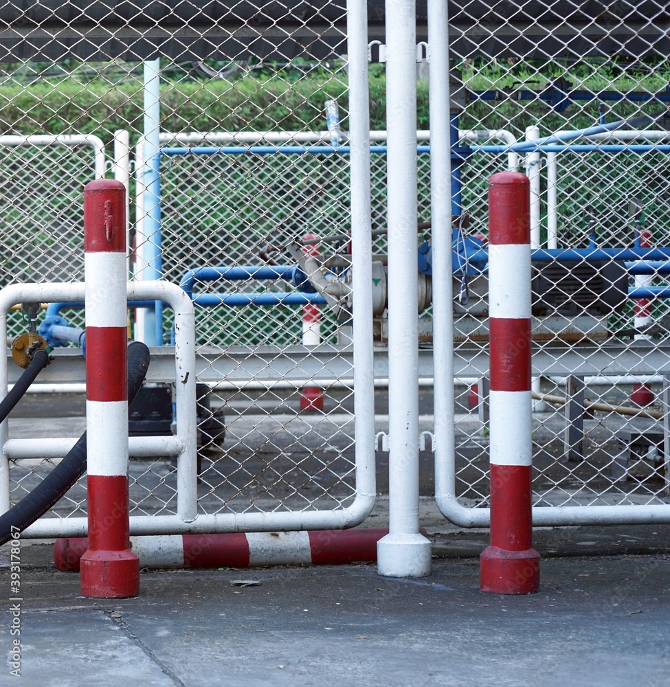A red-white pillars to sign danger  with a steel mesh fence of the gass storage sevice for a car.