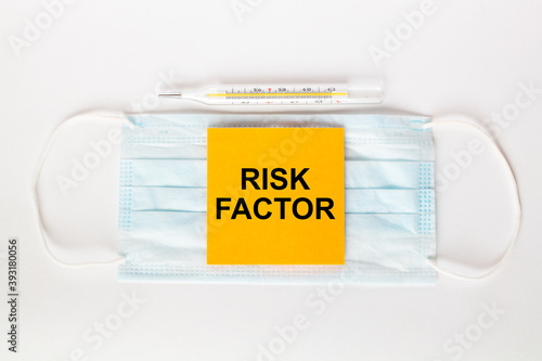 Sticker with text Risk Factor lying on the mask with a thermometer