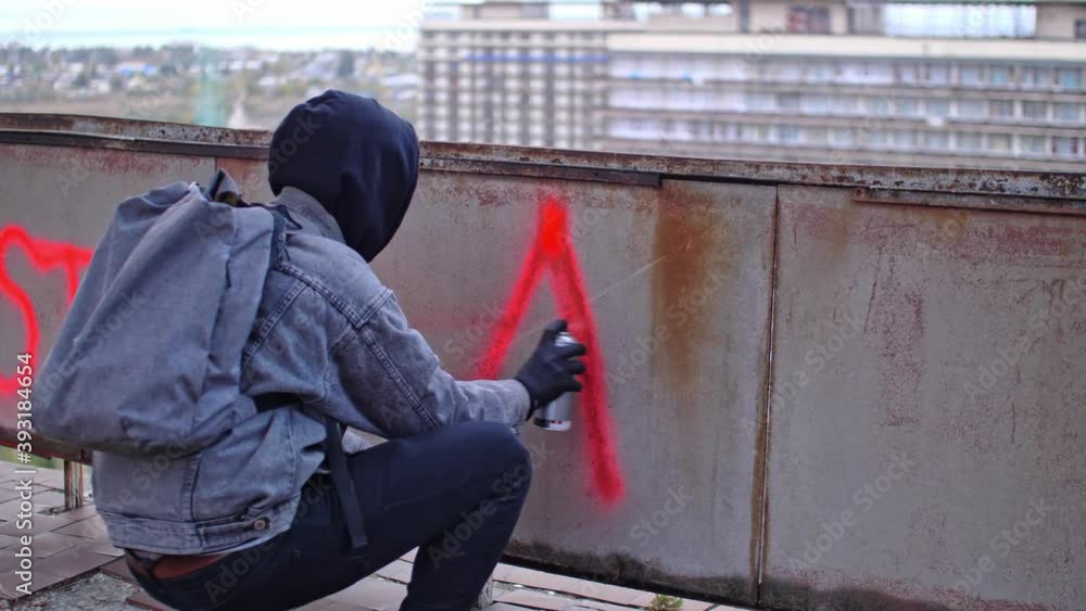 Process of making anarchy graffiti by young protester in a hood with red spray paint Process of making anarchy graffiti by young protester in a hood with red spray paint