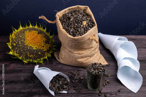 Sunflower and a sack of unpeeled fried seeds with a measuring glass and paper bags. Accessories of a street vendor of sunflower seeds.