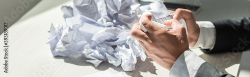 Cropped view of businessman with hands near pile of crumbled papers on blurred background, banner