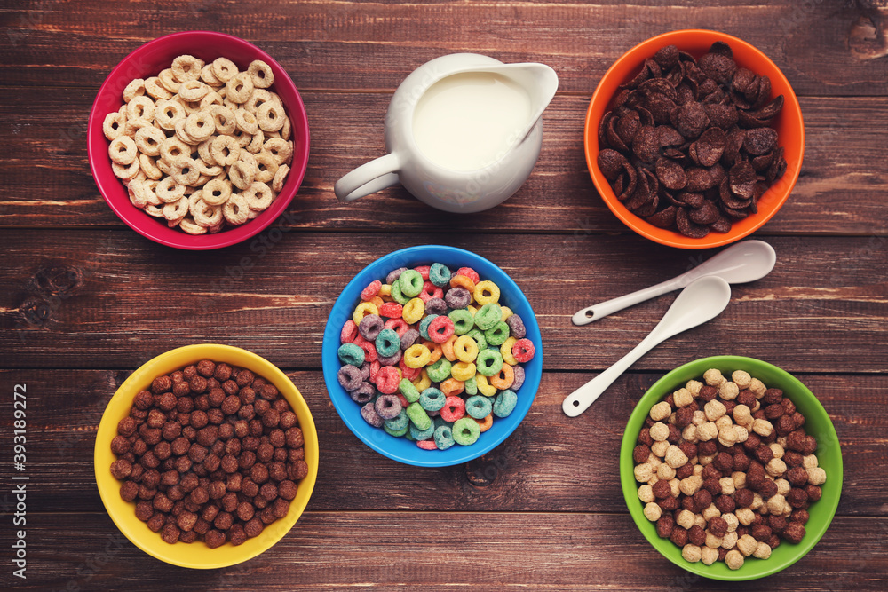 Various corn flakes with milk in jar and spoons on brown wooden table Various corn flakes with milk in jar and spoons on brown wooden table