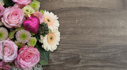 bouquet of roses on the left with a pink heart bauble on wooden background - copy space