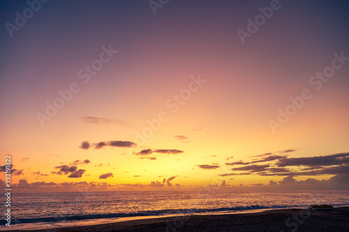 Dramatic sea shore sunset with sun setting down at the cloudy skyline with orange and vivid blues.