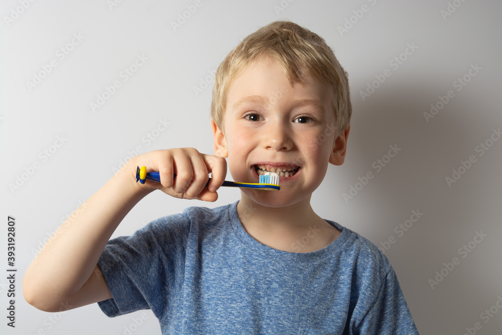 a boy with white hair holds a toothbrush in his hands wants to brush his teeth. gray background. a boy with white hair holds a toothbrush in his hands wants to brush his teeth. gray background.