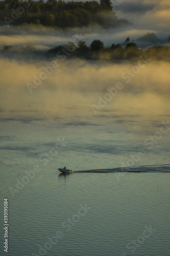 BOAT FLOATS ON THE RIVER THROUGH FOG