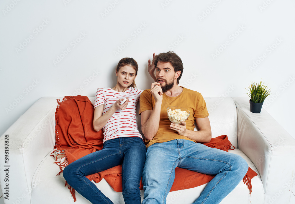 Couple in love with popcorn and watching TV while on the couch indoors Couple in love with popcorn and watching TV while on the couch indoors