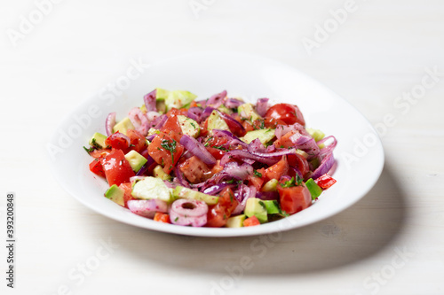 vegetable salad with  red onion, tomato, cucumber, avocado, dill, sumach, paprika, olive oil  in white bowl on wooden table