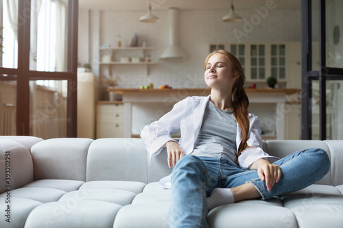 Smiling woman with closed eyes on sofa at home, enjoying lazy weekend alone in own apartment.