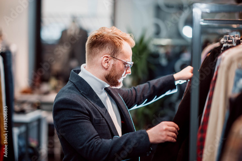 blonde millennial man in a business attire chooses clothes in a store. The man is shopping.