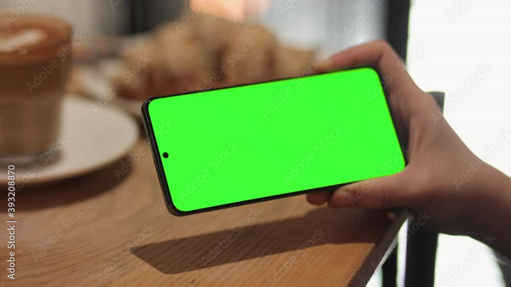 Back View of Female is scrolling, swiping her Smartphone with Green Screen, Chroma Key. Young Woman is Using Cell Phone at Restaurant, holding in Horizontal Position. Surfing Social Media. Back View of Female is scrolling, swiping her Smartphone with Green Screen, Chroma Key. Young Woman is Using Cell Phone at Restaurant, holding in Horizontal Position. Surfing Social Media.