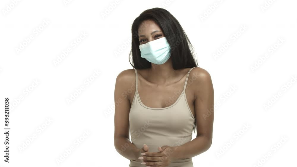 Quarantine, coronavirus and social distancing concept. Attractive african american woman with long dark hair, wearing tank-top and medical mask, smiling and standing shy over white background