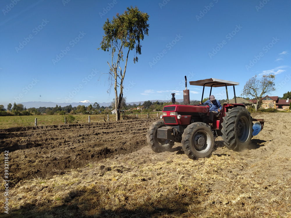 Fototapeta Tractor in a field with a mountain view