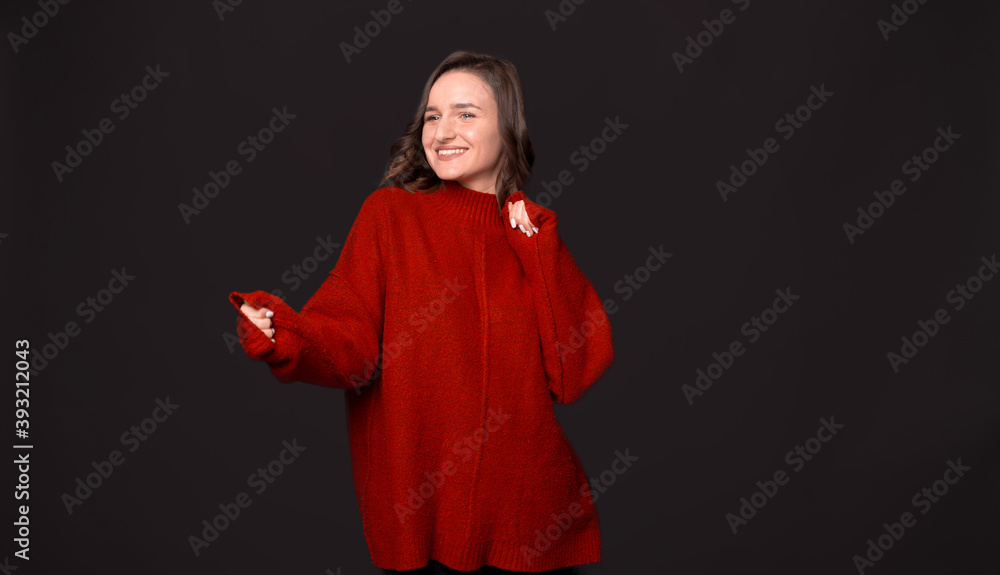 Fototapeta premium Photo of happy young woman in red sweater dancing over dark background
