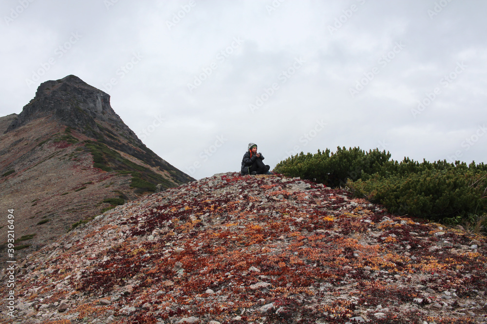 Woman photographer sits surrounded by rocks and mountains, waiting for the moment for a successful shot