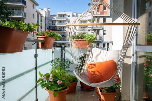 Fototapeta a sunny balony with flowers and potted plants and hammock with orange pillow