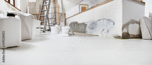 Low angle of indoor shot of construction or building site of home renovation with tools with paint buckets and primer jerry can on white floor with copy space photo