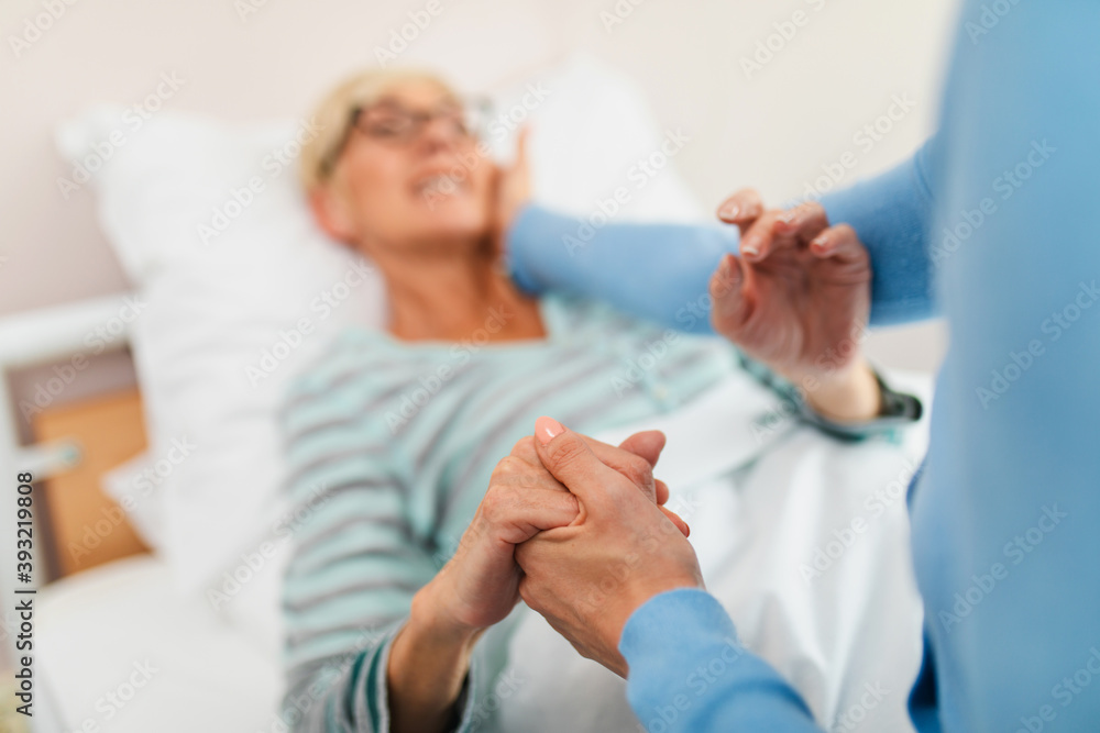 Beautiful middle age woman spending some time with her mother in hospital or nursing center. Senior woman lying in bed. Beautiful middle age woman spending some time with her mother in hospital or nursing center. Senior woman lying in bed.