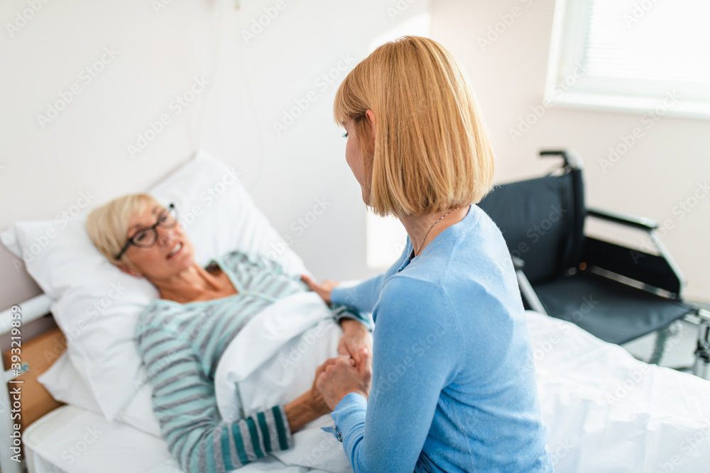 Obraz premium Beautiful middle age woman spending some time with her mother in hospital or nursing center. Senior woman lying in bed.