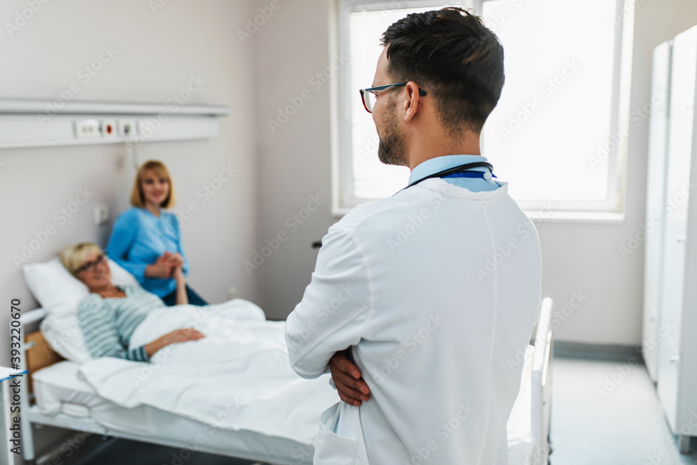 Obraz premium Young doctor visiting sick senior woman with her daughter in hospital room or nursing center.