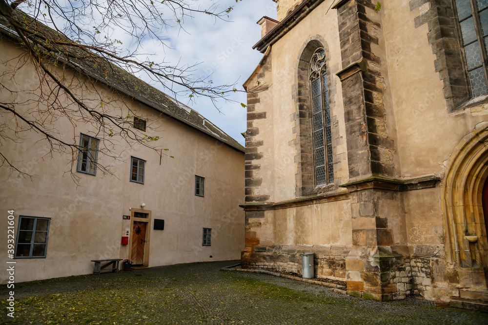 Old school building and medieval gothic catholic church of Saints Peter and Paul near castle Melnik in sunny autumn day, High clock tower, Central Bohemia, Czech republic