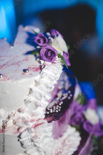 Vertical shot of a three-floor cake decorated with purple flowers with a blurry background photo