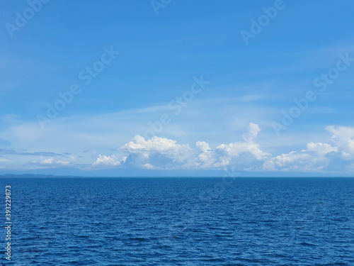 Calm atmosphere of ocean waves with clouds and horizon and deep blue sky. The summer seascape and sky background 