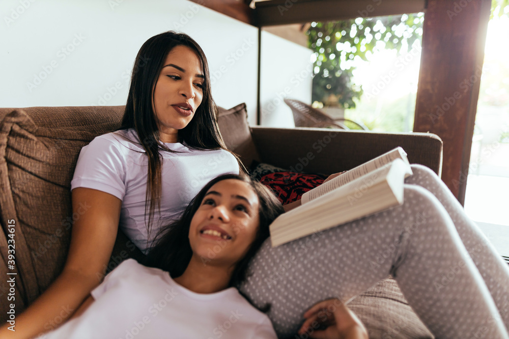Latin mother and daughter reading a book together on the couch in the morning Latin mother and daughter reading a book together on the couch in the morning