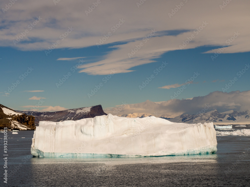 Large white iceberg in Antarctica with land, blue sky and white cloud background