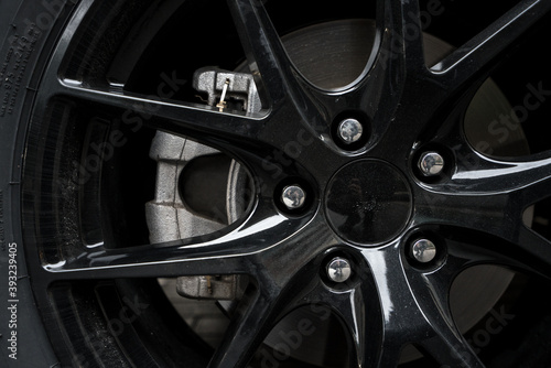 Image of a car tire fitted with black alloy rims  and view of the brakes