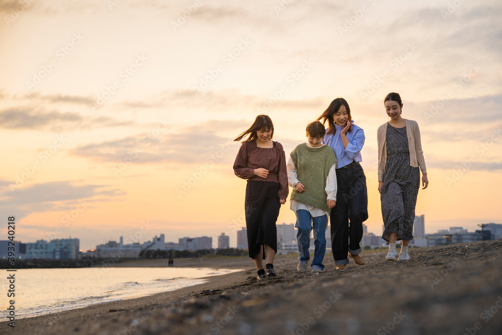 Fototapeta premium 夕暮れの中、寄り添って海沿いを歩く女性4人