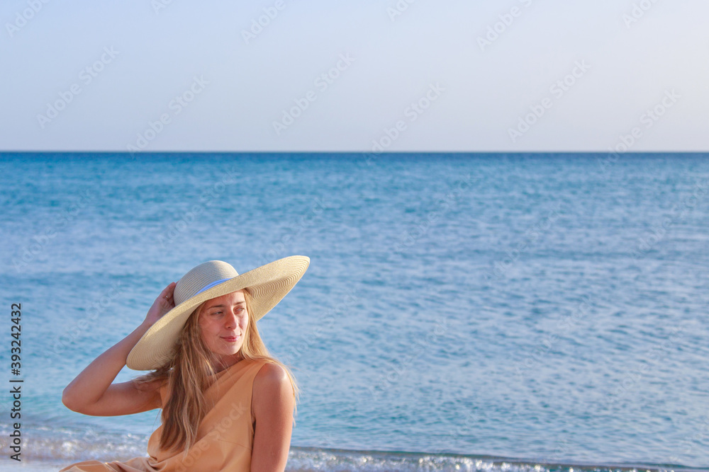 journey to the sea. a girl in a yellow dress and hat is walking along the beach. a tourist walks along the sea coast. hot trips during the holiday period. copy space