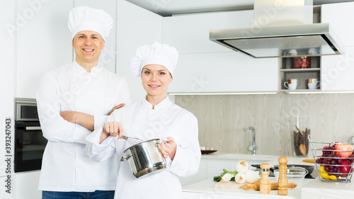 Portrait of the woman and man professionals who are posing with devices in the kitchen at the cafe.