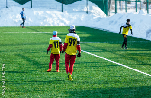 Boys in gray yellow sportswear running on soccer field with snow on background. Young footballers dribble and kick football ball in game. Training, active lifestyle, sport, children winter activity © Natali