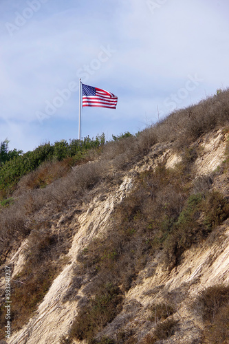 Low angle view of an United States flag waving high on top of the bluffs at a southern California Pacific ocean beach on a warm autumn day